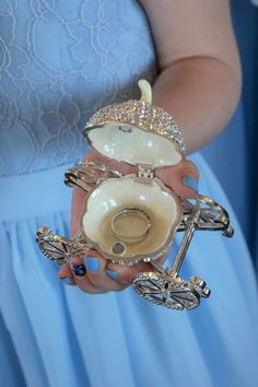 a woman in a blue dress holding a white ring holder with two rings on it