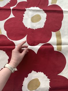 a hand pointing at a red and white flower design on a sheet with gold dots