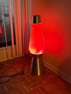 a red light shines on the floor next to a lamp in front of a window