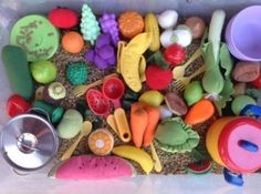 an assortment of plastic toys in a container with spoons and other items on the floor