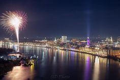 fireworks are lit up in the night sky over a river and cityscape with buildings