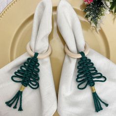 two white napkins with green tassels are on a plate next to flowers