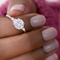 a woman's hand with a diamond ring on top of her finger and the other hand holding an engagement ring