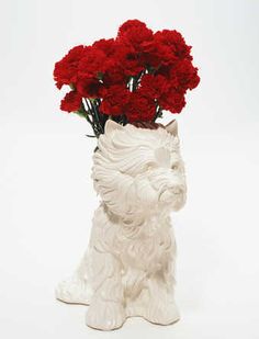 a white vase with red carnations and a dog figurine in it