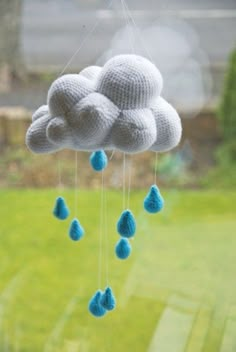 a crocheted cloud mobile hanging from a window with raindrops on it