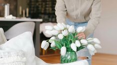 a woman arranging white tulips in a vase