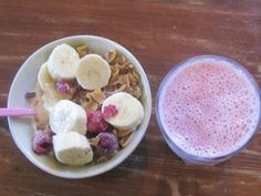 a bowl of cereal with bananas and raspberries next to a glass of milk