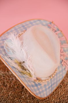 Introducing THE AUDRA RANCHER HAT - a playful twist on the classic cream rancher hat. This unique hat features gold accents and a stylish blue gingham pattern. With a gold chain band and pink bows, it's the perfect mix of chic and quirky. Plus, the white feather combo adds a touch of whimsy. Get ready to turn heads and stand out from the crowd! This hat is ONE OF A KIND, created by our owner Stephanie. To receive item quicker, expedited shipping is available at checkout. Hat Bar, Rancher Hat, Unique Hats, Pink Bows, White Feather, Gingham Pattern, Hat Ideas, White Feathers, Blue Gingham