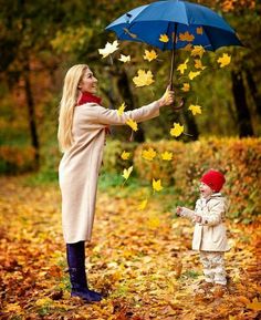 a woman holding an umbrella next to a little boy in the woods with autumn leaves