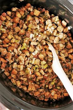 a wooden spoon in a crock pot filled with stuffing and vegetables, ready to be cooked