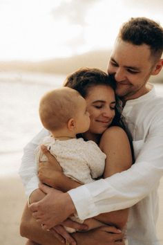 a man and woman holding a baby on the beach