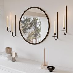 a round mirror hanging on the wall above a mantle with candles and other items in front of it