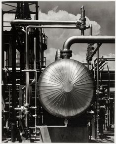 an industrial gas plant with pipes and tanks in the foreground, against a cloudy sky