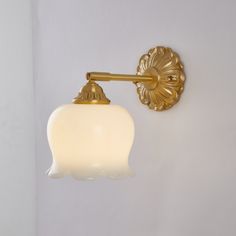 a wall light that is on the side of a white wall with a gold finish