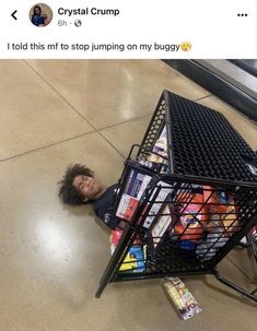 a child is laying on the floor next to a shopping cart with books in it