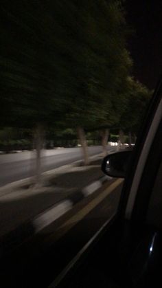 blurry image of cars driving down the road at night time with trees in the background