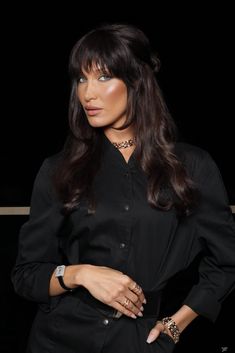 a woman with long dark hair wearing a black shirt and leopard print bracelets, posing for the camera