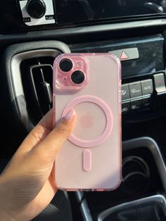 a person holding up a pink phone case in their car with the steering wheel visible