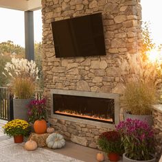 a stone fireplace with a flat screen tv mounted on it's wall next to potted plants and pumpkins