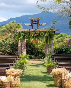 an outdoor ceremony set up with wooden benches and wicker baskets filled with flowers on the grass