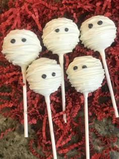 four cake pops with white frosting and black eyes on them sitting on red shredded paper