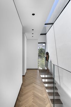 there is a woman standing on the stairs in this modern house with white walls and wood flooring