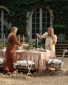 two women standing around a table with food on it and candles in the air above them