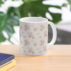 a white coffee mug with pink flowers on it sitting on a table next to some books