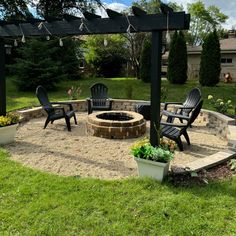 an outdoor fire pit surrounded by lawn chairs and potted plants in the middle of a yard