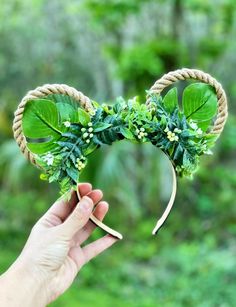 a hand holding up a mickey ears headband with greenery on it's side