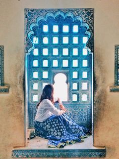 a woman sitting on a ledge in front of a window with blue and white tiles