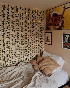 an unmade bed in front of a wall with ivy on it and pictures above