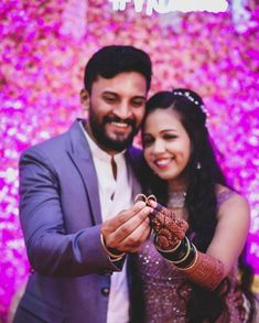 a bride and groom holding their hands together in front of a flower wall with the word love written on it