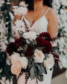 a bride holding a bouquet of red and white flowers with greenery around her neck