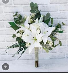 a bouquet of white flowers and greenery in front of a brick wall