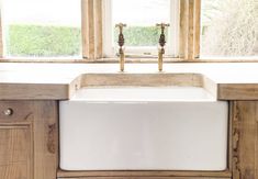 a white sink sitting under a window next to wooden cabinetry in a room with lots of windows