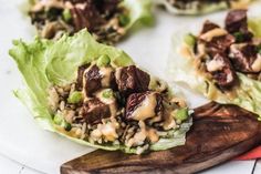 lettuce wraps filled with meat and dressing on top of a wooden cutting board