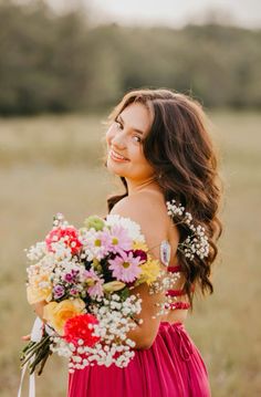 a woman in a red dress holding a bouquet of flowers and smiling at the camera