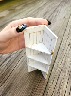 a hand holding an open shelf on top of a wooden floor next to a black and white nail polish