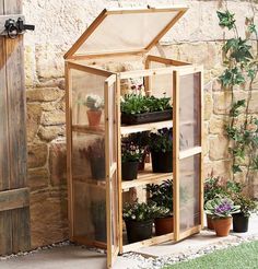 a small greenhouse with potted plants in front of an old stone wall and wooden door