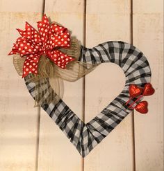 a heart shaped wreath with red bows and plaid ribbon hanging on a white wooden wall