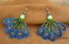 peacock feather earrings with green bead and blue beads on the end, sitting on a tan surface