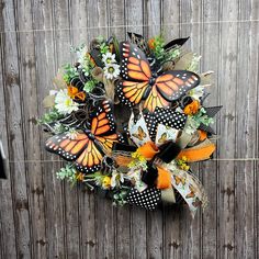 an orange and black butterfly wreath on a wooden fence next to a door with flowers