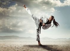 a woman is doing karate in the middle of a desert area with mountains and clouds behind her