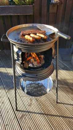 a grill with hot dogs on it sitting on a wooden deck next to a fence