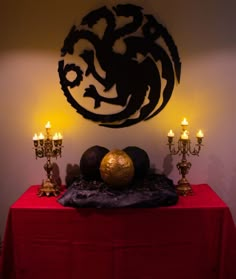 a red table topped with candles next to a wall mounted dragon sculpture on top of it