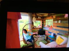 a woman sitting in a hanging chair next to a window with colorful wood planks on the walls