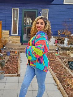 a woman standing on the sidewalk in front of a blue house wearing jeans and a colorful sweater