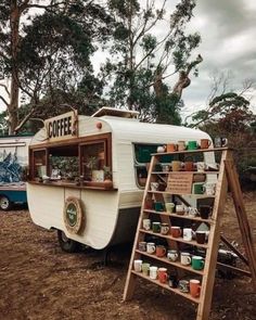 an old camper is parked next to a sign with coffee written on it and shelves full of cups