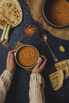 a person holding a bowl of soup next to some pita bread and other food